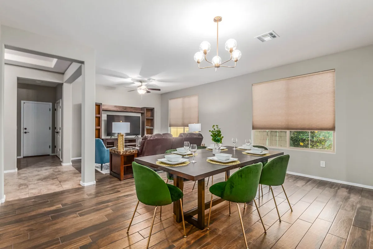 This image captures a spacious open-concept living and dining area. In the foreground, a stylish dining table with green chairs seats six, while the background reveals a cozy living zone with a television—perfect for relaxing or socializing. Natural light pours in, enhancing the inviting feel and highlighting the seamless flow between the spaces.