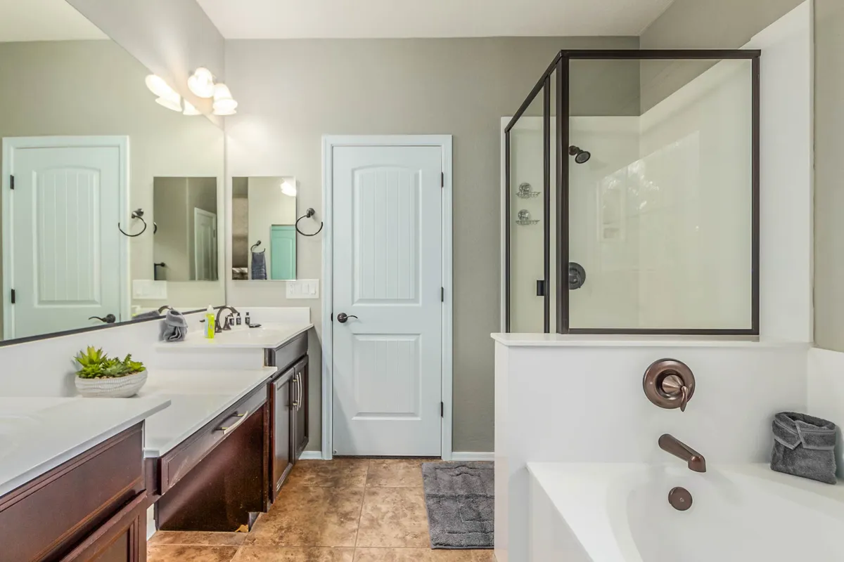 A spa-like ensuite bathroom featuring double sinks, framed mirrors, a glass-enclosed shower, and a freestanding bathtub. The design is fresh and serene, reflecting the feeling of luxury and rejuvenation mentioned in the text.