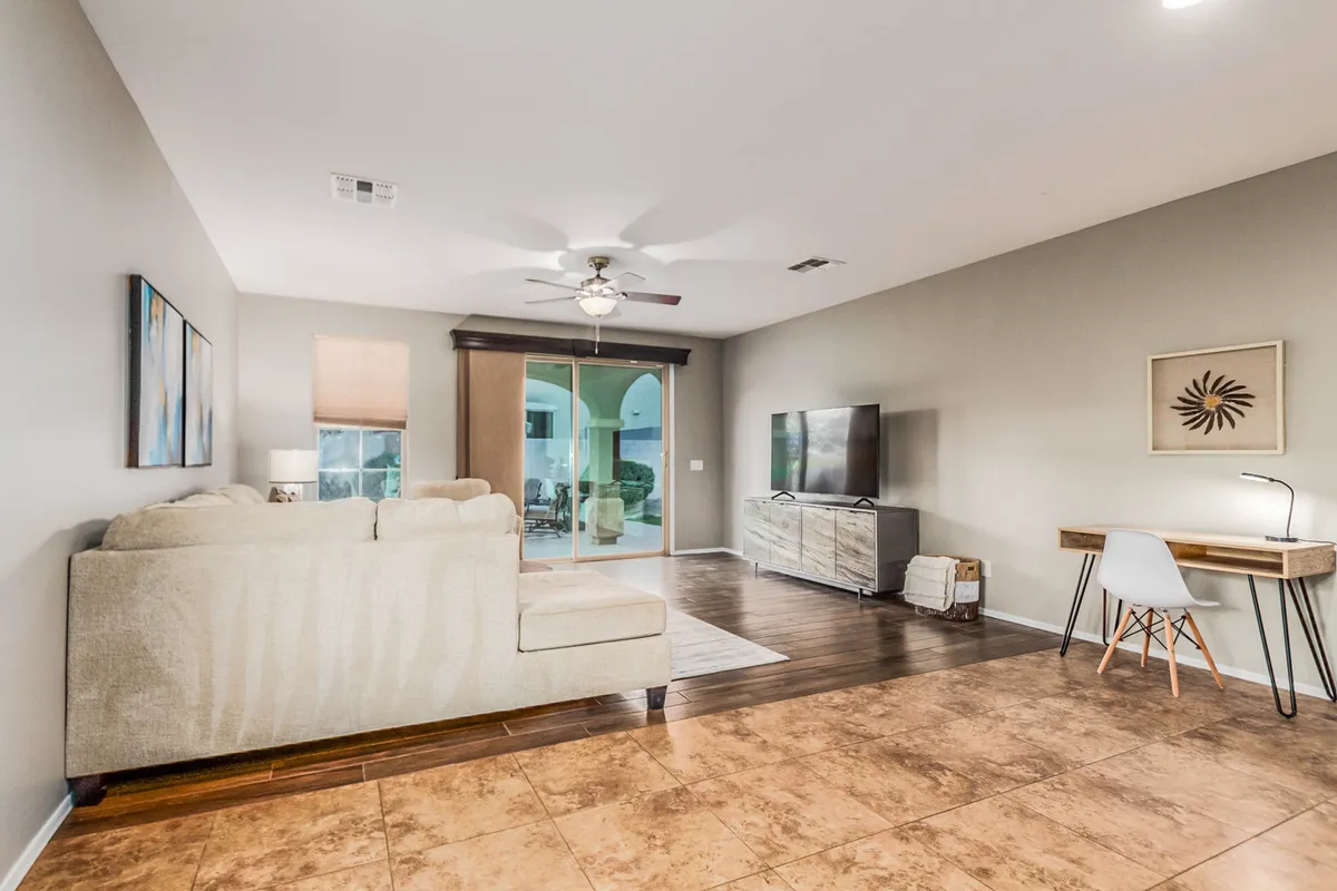 A comfortable living area featuring a plush sofa, a television mounted near sliding glass doors, and a compact workspace. The space feels cozy and well-lit, making it ideal for unwinding after a busy day or enjoying family time.
