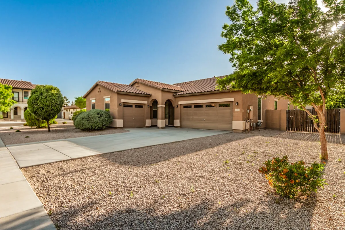 A wide exterior view of the property's front entrance, driveway, attractive landscaping, and garage doors. The inviting setting provides a sense of arrival and hints at the property's connection to the neighborhood and community walking paths.