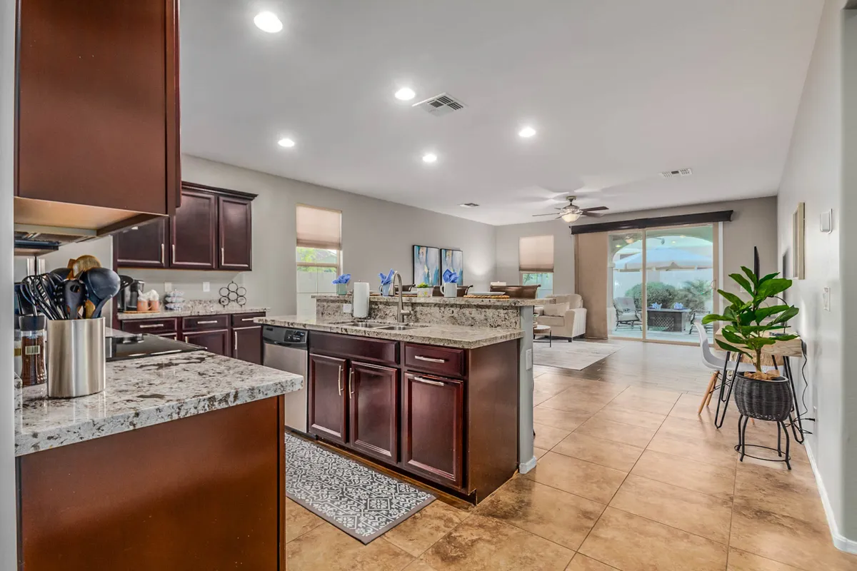 This angle reveals a kitchen with a granite countertop, dark wood cabinetry, comfortable bar seating, and large windows flooding the area with natural light. The image hints at a relaxed, sociable environment ideal for casual meals and productivity.
