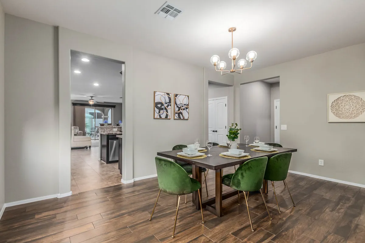 A stylish dining area featuring a large table surrounded by green chairs, illuminated by a modern chandelier. The setting is arranged for communal dining and socializing, highlighted by tasteful wall art that adds color and vibrancy to the space. The welcoming atmosphere invites groups to gather for meals and celebrations.