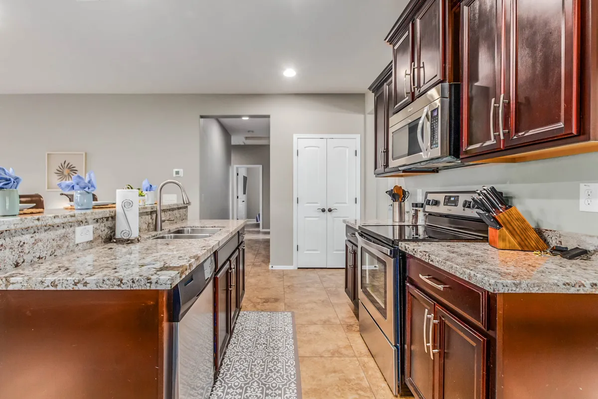 This image showcases a modern kitchen with striking granite countertops, dark wood cabinetry, and gleaming stainless steel appliances. The space is bright and inviting, with a decorative rug adding warmth, and the open layout suggests easy flow into adjacent living areas.