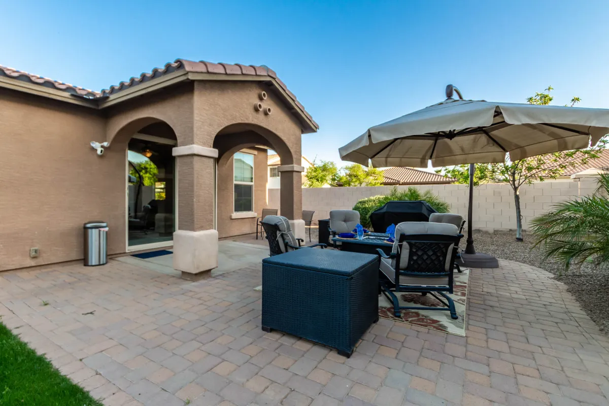 A relaxed patio scene featuring patio furniture, an umbrella for shade, an outdoor rug, and vibrant potted plants. The space is set up for outdoor dining, entertaining, and enjoying the Arizona weather with friends and family.